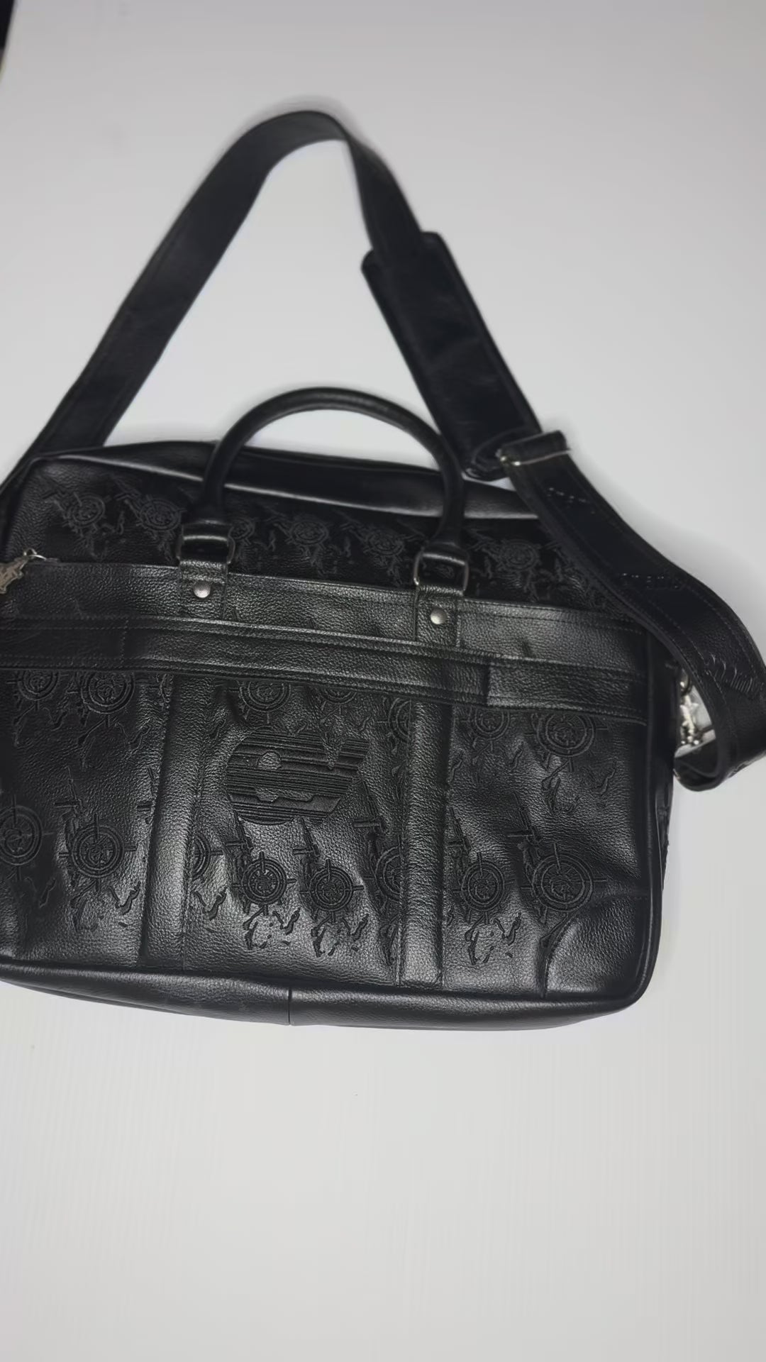 Detail video of Veil For Liberty black leather 
briefcase showing embossed monogram pattern, 
silver hardware and Enamy charm. Maison Enamy NYC.