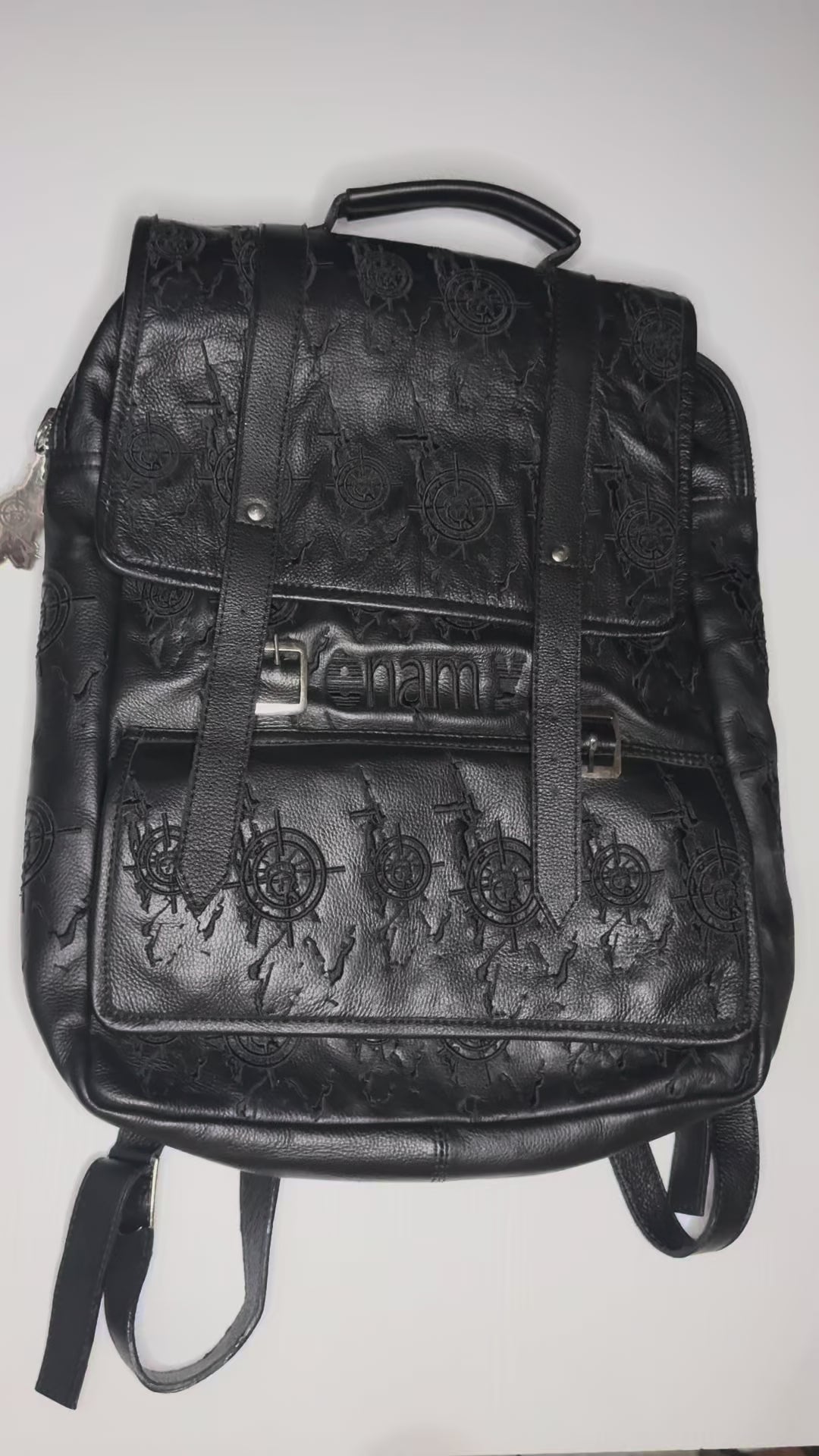 Detail video of black genuine leather backpack 
showing embossed Veil For Liberty monogram brass 
buckles padded straps and Enamy charm zipper pull.