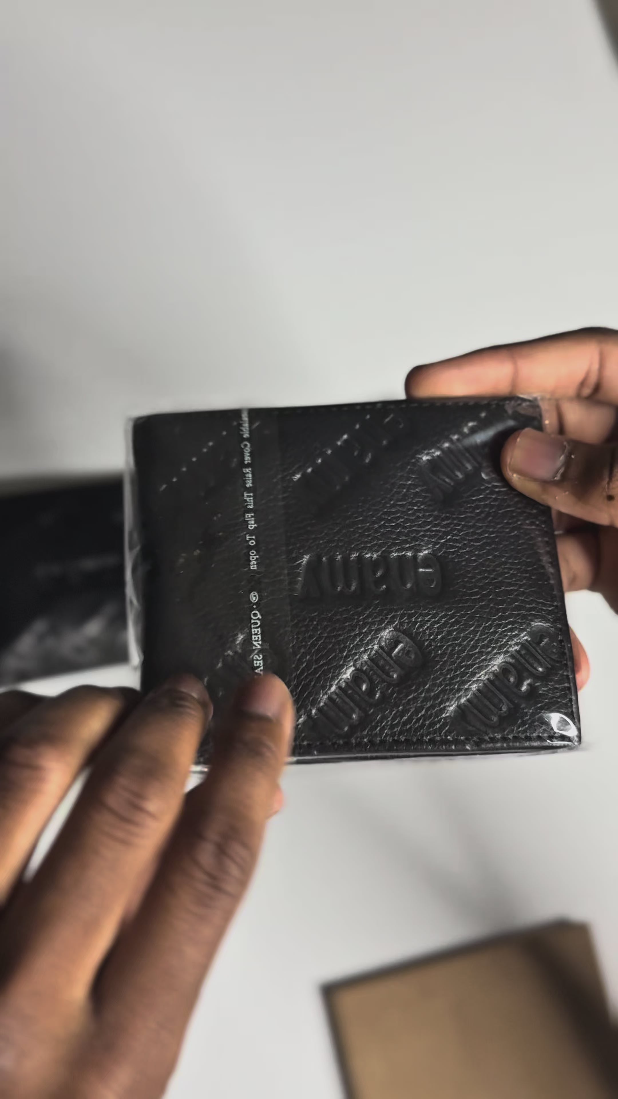Detail video of Enamy Monogram black genuine 
leather bifold wallet showing embossed pattern 
and leather texture. Maison Enamy NYC.